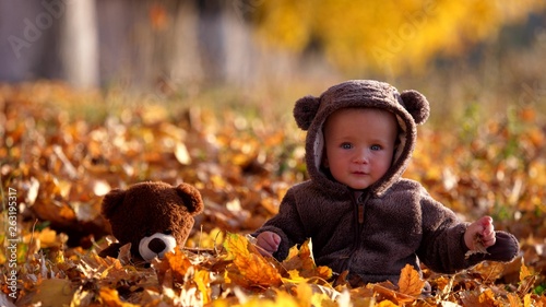 Amusing baby and teddy bear toy sit on autumn foliage and play with leaves  early friendship