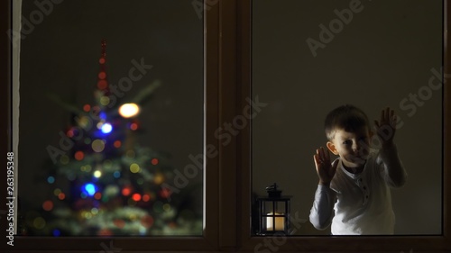 Funny child look careful on window in the night for Santa Claus coming, Christmas tree, waiting big celebration, conceptual
