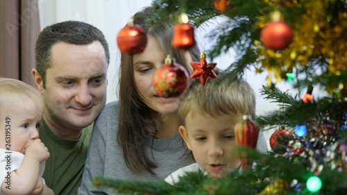 Family decorate together Christmas tree, baby, brother and young parents, celebration of joy © MEDIAIMAG