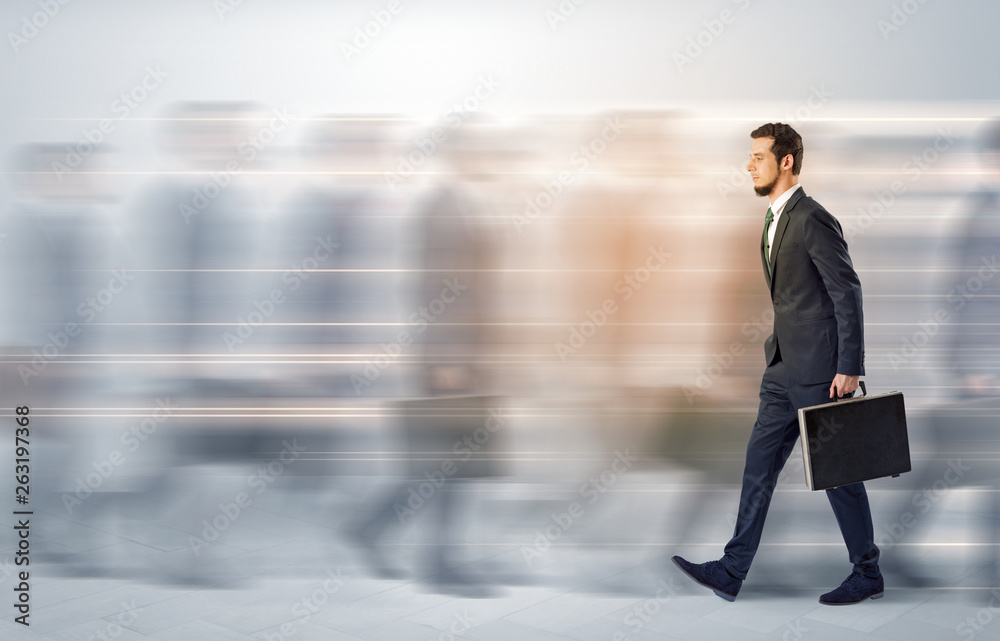 Obraz premium Young businessman with briefcase hurry up on a crowded street with blurred people around 