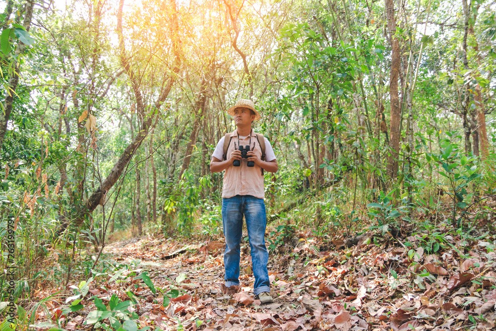 Young man with backpack and holding a binoculars walking on trail in forest