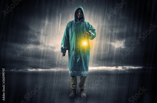 Raincoated man walking in storm with glowing lantern in his hand 