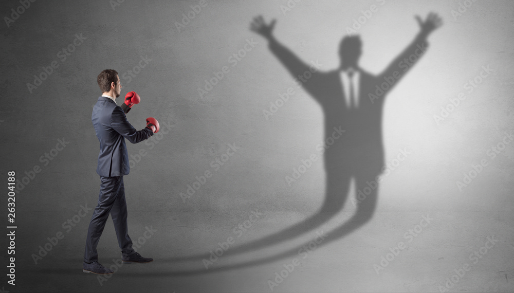 Fototapeta premium Businessman with boxing gloves fighting with disarmed businessman shadow 