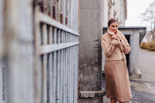 young stylish cute girl in a fur coat strolling around the city near wooden houses and stone walls