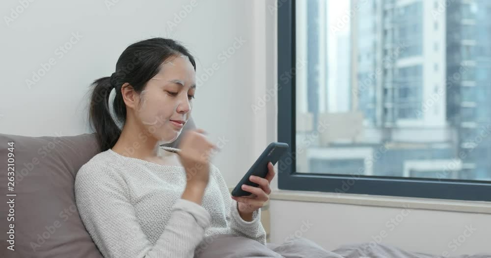 Woman apply face mask and watch on cellphone on bed Woman apply face mask and watch on cellphone on bed