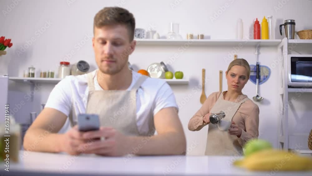 Handsome man typing message in phone, jealous wife peeking, cheating in marriage Handsome man typing message in phone, jealous wife peeking, cheating in marriage