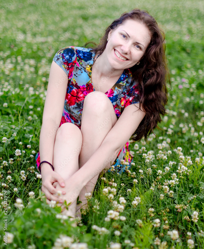 Soft portrait of happy and attractive young caucasian woman in nice dress on the lawn with clover flowers in the summer park. Soft portrait of happy and attractive young caucasian woman in nice dress on the lawn with clover flowers in the summer park.