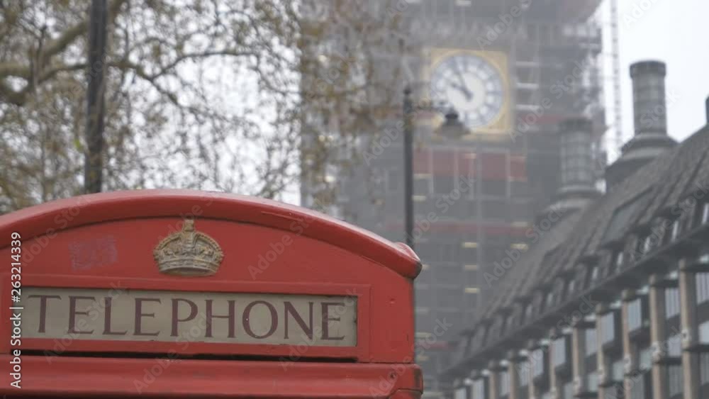 A top of a red phone booth and Big Ben clock covered in scaffolding. A top of a red phone booth and Big Ben clock covered in scaffolding.