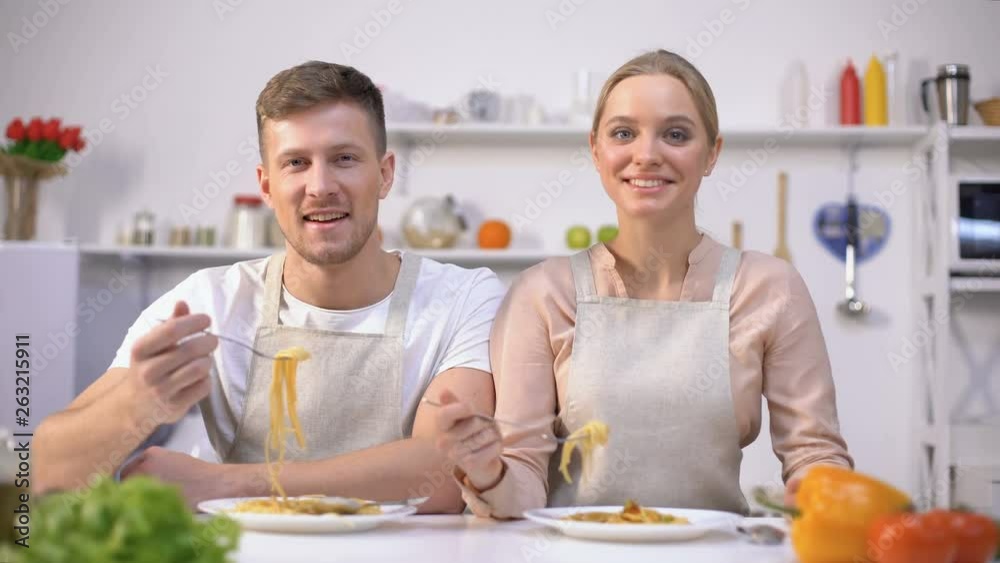 Young couple eating pasta, smiling on camera, concept of quick and easy food Young couple eating pasta, smiling on camera, concept of quick and easy food