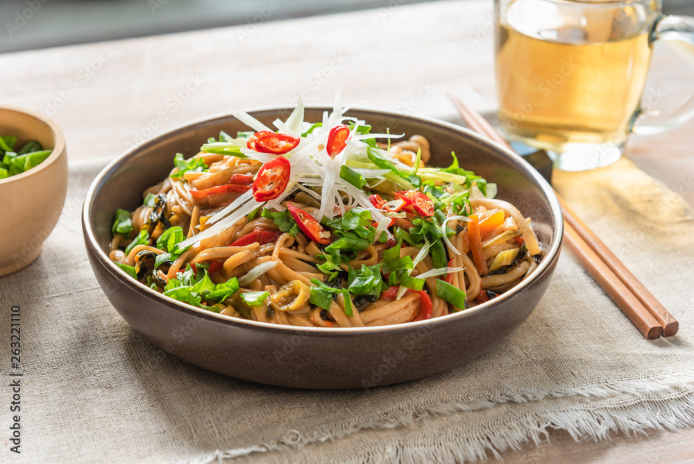 Asian vegan lunch - spicy chow mein noodles with carrots, pepper and spinach with sliced radish, spring onions and chili peppers on a rustic table - obrazy, fototapety, plakaty 