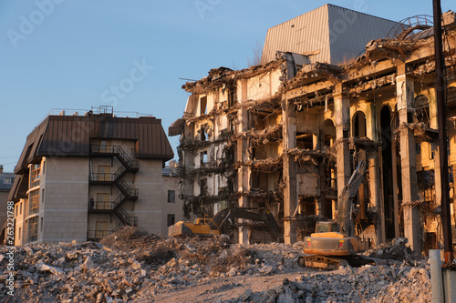 Building demolition with hydraulic excavator. Dismantle of destructed house ruins at bright sunsest
