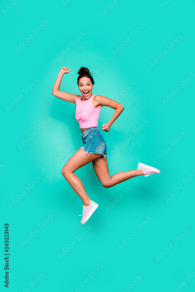 Vertical full length body size photo beautiful she her stylish trendy hairdo jump high win winner victory achievement wear casual pink tank-top jeans denim shorts isolated teal turquoise background