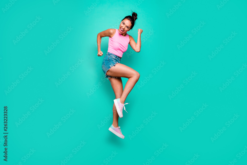 Full length side profile body size photo beautiful she her trendy hairdo jump high yell scream shout yeah wild roar wear casual pink tank-top jeans denim shorts isolated teal turquoise background Full length side profile body size photo beautiful she her trendy hairdo jump high yell scream shout yeah wild roar wear casual pink tank-top jeans denim shorts isolated teal turquoise background