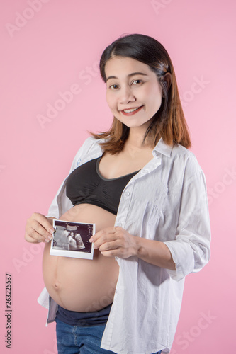 cute pregnant belly and x-ray ultrasound scan of baby. Pregnant female motherhood concept. Side view, pregnant belly body part. Third trimester on pink background