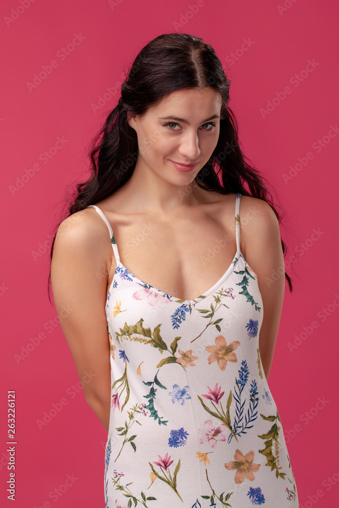 Portrait of a pretty young woman in a light dress standing on pink background in studio. People sincere emotions.