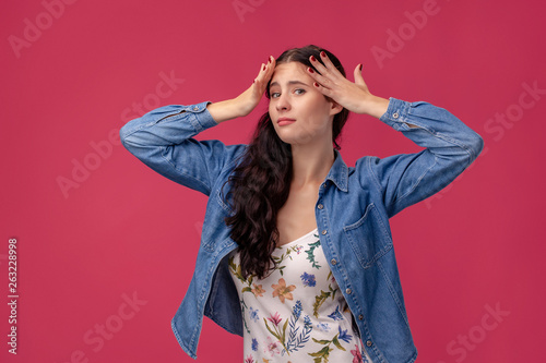 Portrait of a pretty young woman in a light dress and blue shirt standing on pink background in studio. People sincere emotions.