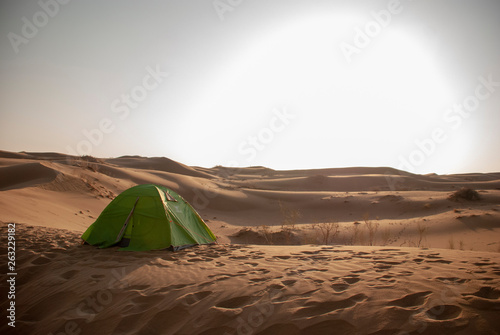 A big sun shines in the sky on a green tent on desert