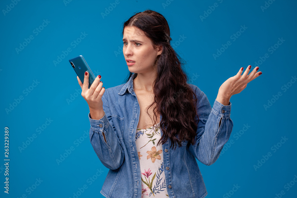 Young brunette woman is posing with a smartphone standing on blue background. Young brunette woman is posing with a smartphone standing on blue background.