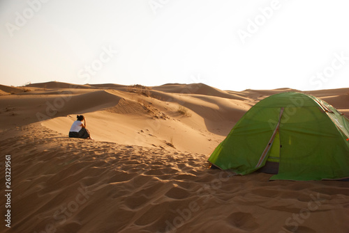A girl sits alone near her tent deep in desert  and looks away