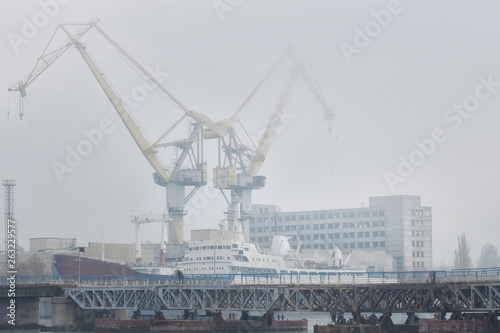 Lifting cargo cranes and ship in sea port. Foggy industrial landscape.