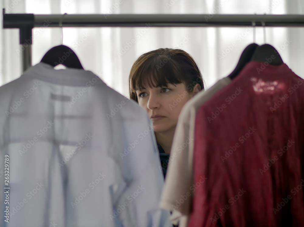Young pretty brunette woman considering clothes on hangers Young pretty brunette woman considering clothes on hangers