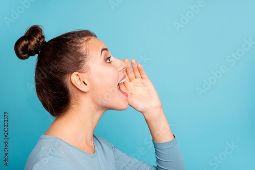 Profile side view photo of funny funky teen teenager shout loud ads novelties place hand near open mouth yell look up dressed modern youngster clothes isolated on blue background photo