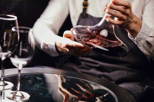 Tableau sur toile Cropped view of professional sommelier holding mixing bowl with red wine in hands over the table in wine restaurant