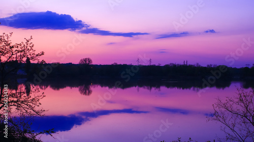 Nice symmetry of clouds reflected in the water of a lake. Very colorful sunrise in a beautiful landscape