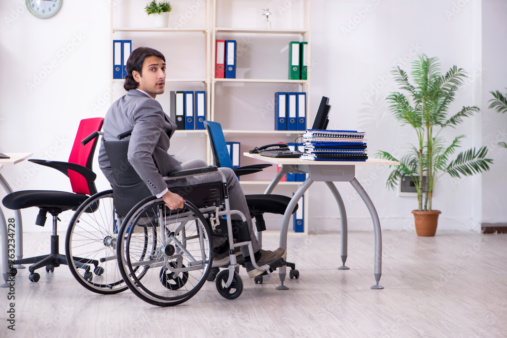 Young handsome employee in wheelchair working in the office Young handsome employee in wheelchair working in the office