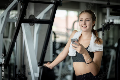 Happy Young attractive women fitness using smartphone resting in gym during morning exercise. Relaxation after hard workout in gym. Healthy sports lifestyle, Fitness concept.