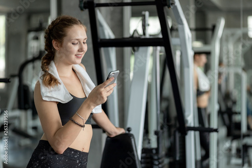 Happy Young attractive women fitness using smartphone resting in gym during morning exercise. Relaxation after hard workout in gym. Healthy sports lifestyle, Fitness concept.