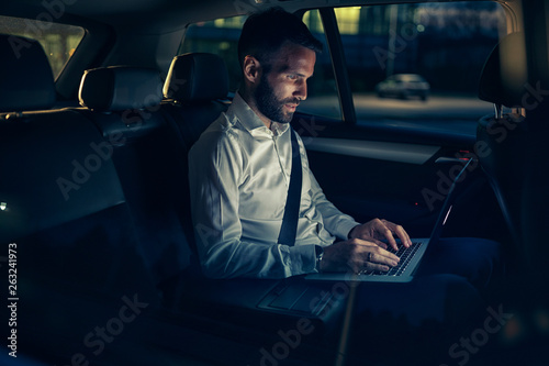 Businessman in car working on laptop in back seat. © luckybusiness