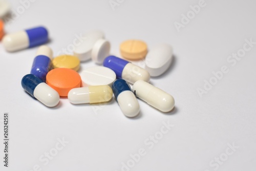A close-up photo of various medical pills and capsules spilt on white background