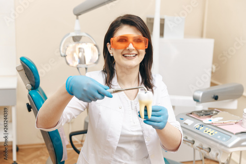 Female dentist in the mask showing how to make tooth filing on the tooth model