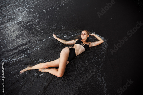 The girl in the swimsuit  lying on the black sand.