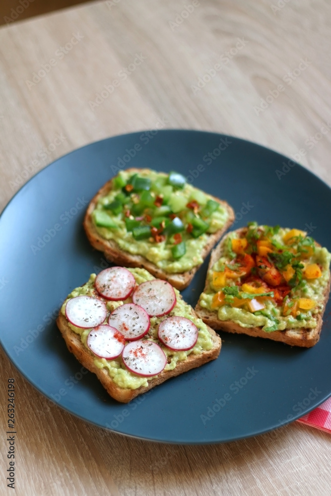 Three slices of toast with mashed avocado and various vegetable and herb toppings. Selective focus. Three slices of toast with mashed avocado and various vegetable and herb toppings. Selective focus.