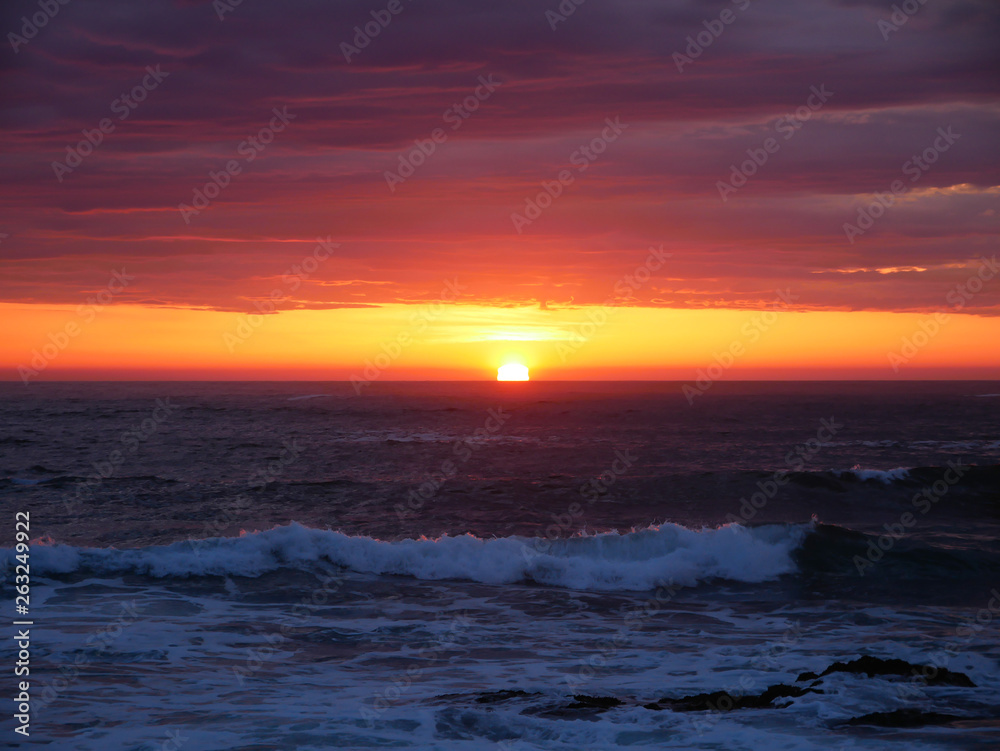 Sun on horizon at sunset on the beach with beautiful vivid orange sky.