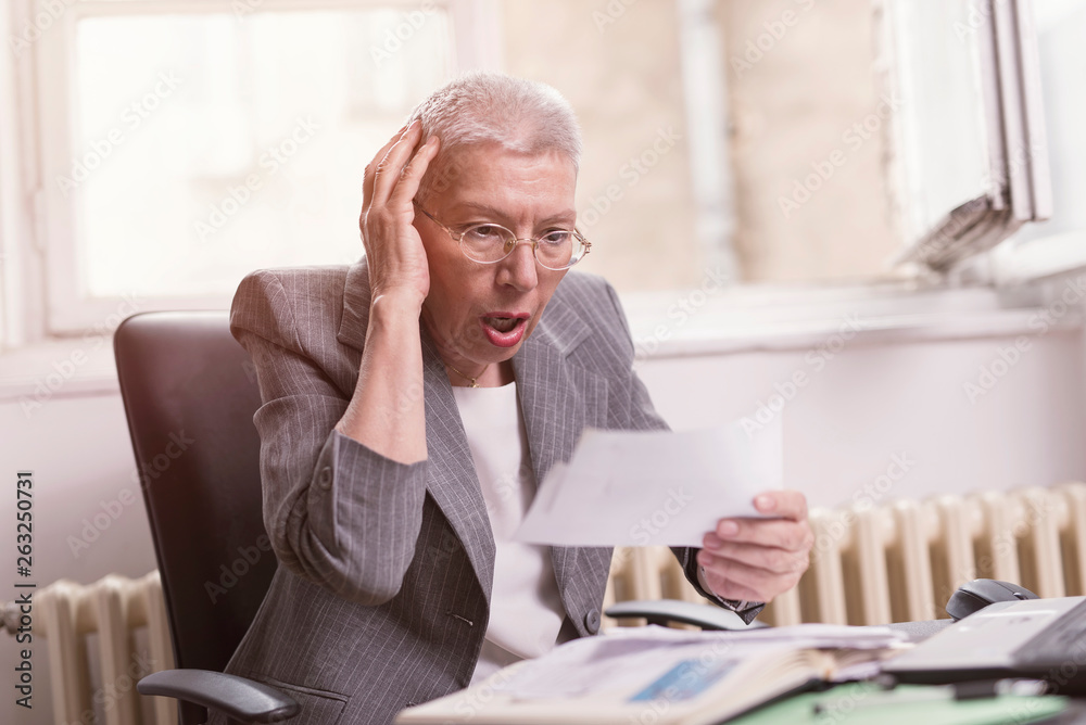 Fototapeta premium Senior old businesswoman shocked with the bills she receives, appalled and gasping