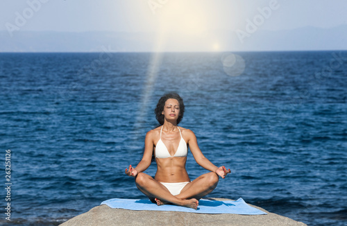 Young brunette woman doing yoga on coast of sea on beach.