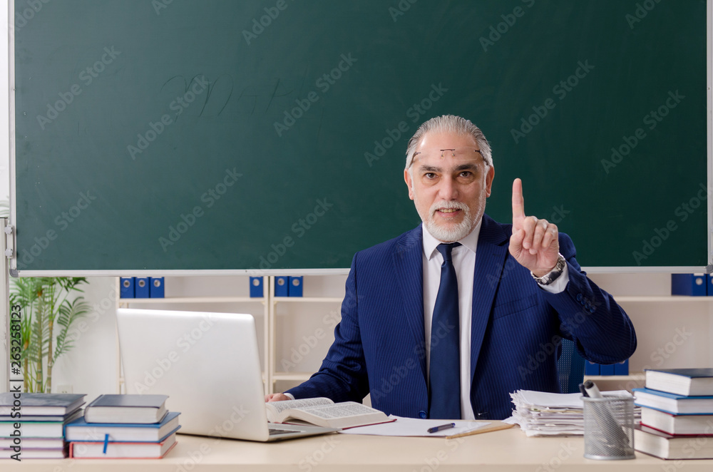 Aged male teacher in front of chalkboard Aged male teacher in front of chalkboard