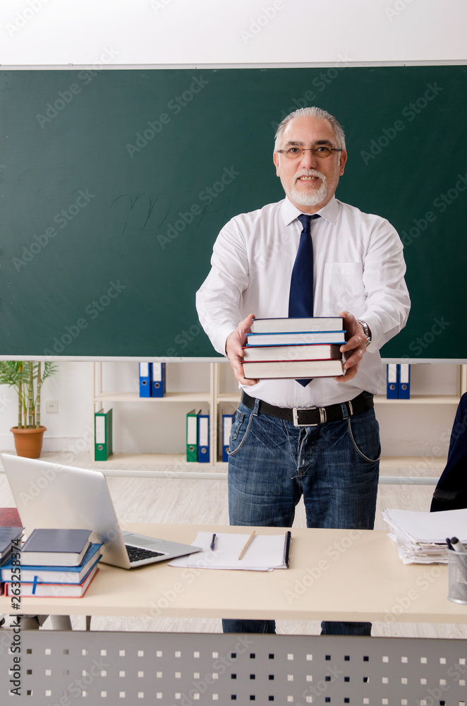 Aged male teacher in front of chalkboard 