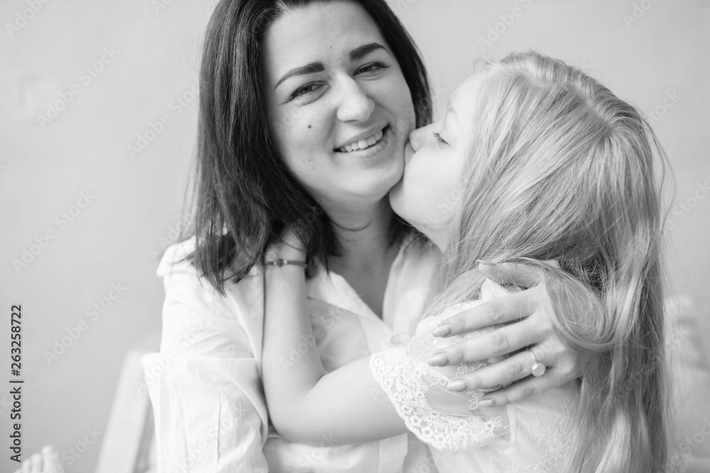 Mother and daughter indoor lifestyle portrait. Mom with child have fun on abstract background. Happiness of motherhood. Mother hugs with her little daughter. Young emotional girl  playing with mom