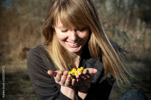 Young European woman holding flowers and smiling. Girl enjoys spring flowers. Happy woman having fun enjoying life