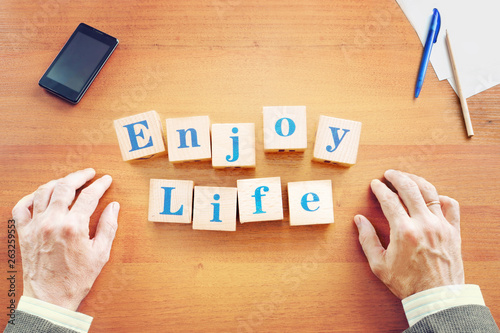 Enjoy life. Businessman made text from wooden cubes on a desk