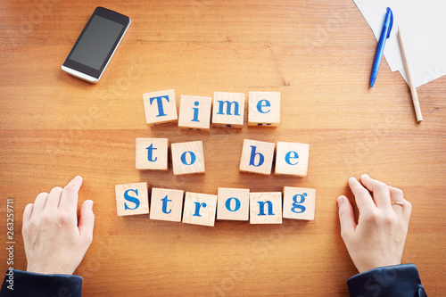 Time to be strong. Business woman made text from wooden cubes on a desk