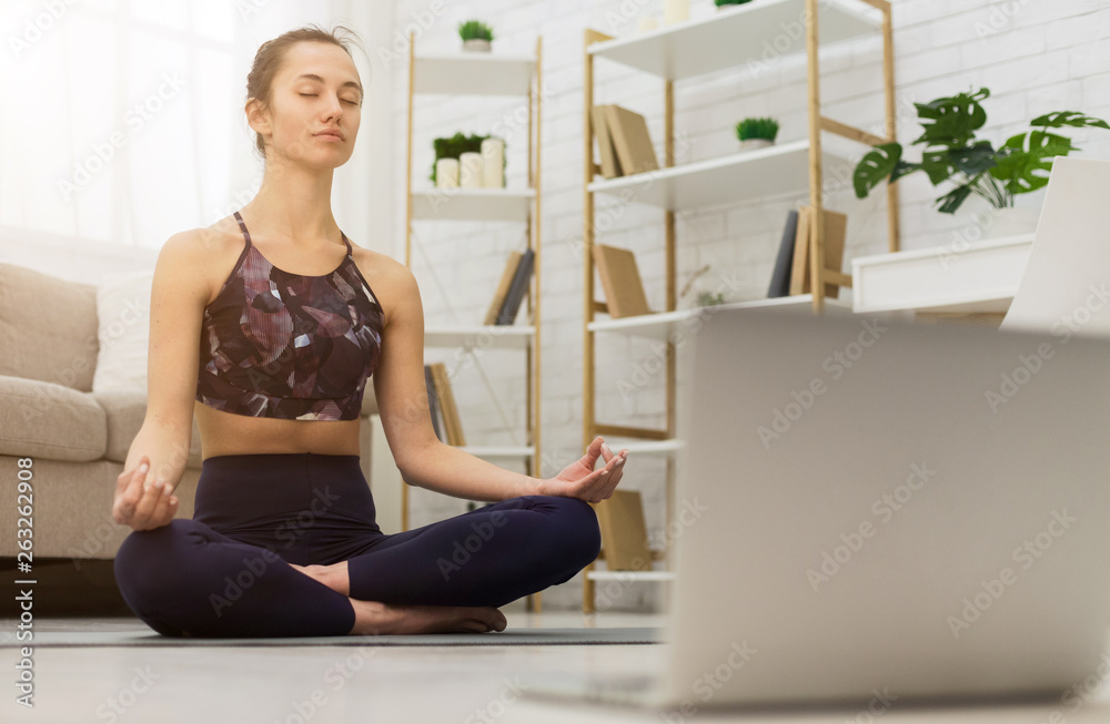 Meditating with laptop. Woman training yoga online