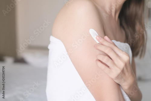 Woman sitting on bed and applying cream lotion on her arm  Beauty Concept.