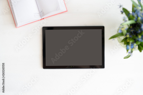 Tablet with black empty screen. Notebook and flowers on table