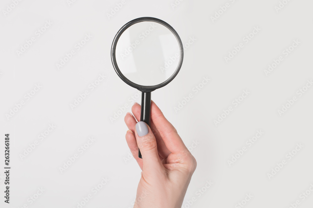Female hand holding magnifier isolate on light background. Female hand holding magnifier isolate on light background.