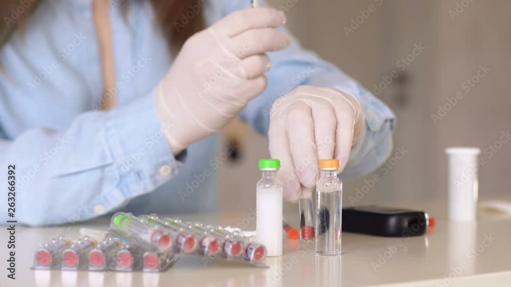 Close-up of a woman in medical gloves is picking up insulin in an insulin syringe, on the table next to it are insulin bottles, a glucometer and syringes. World Diabetes Day. Close-up of a woman in medical gloves is picking up insulin in an insulin syringe, on the table next to it are insulin bottles, a glucometer and syringes. World Diabetes Day.